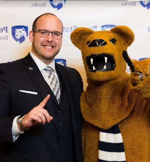 A person stands with the Nittany Lion, both hold up their index fingers